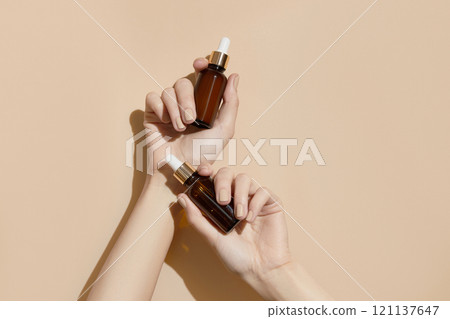 A womans hands holding a brown bottles of serum on a beige background. Body care A womans hands holding a brown bottles of serum on a beige background. Body care 121137647