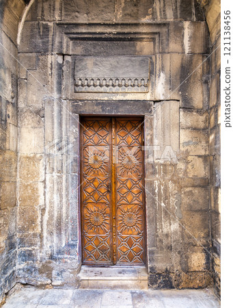 Intricately carved wooden door in an ancient stone wall of a historical building 121138456