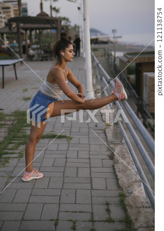 A woman performing a stretch by the waterfront, enjoying the beautiful coastal scenery 121138754