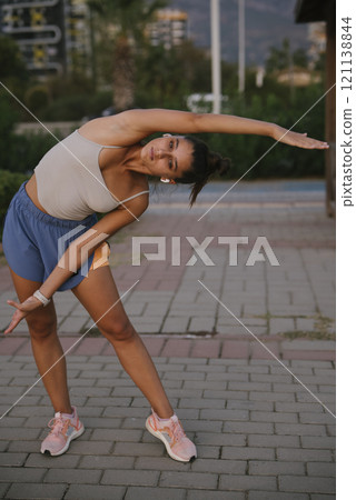 A Young Woman Engaging in Stretching Exercises Outdoors While Dressed in Stylish Athletic Wear 121138844