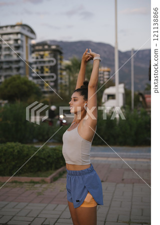 AYoung Woman Stretching Outdoors in Stylish Sportswear Beneath a Beautiful Sunlit Sky AYoung Woman Stretching Outdoors in Stylish Sportswear Beneath a Beautiful Sunlit Sky 121138866