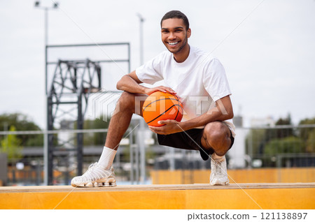 Handsome dark-haired young basketball player with a ball looking happy 121138897