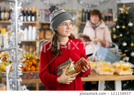 Pretty young european girl purchaser choosing sweets in grocery store decorated for New Year holiday 121138937