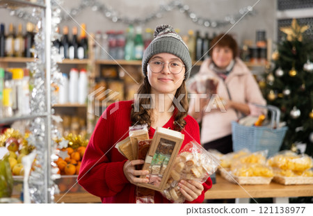 Adolescence girl customer choose nougat, aunt companion in background with shop basket trolley Adolescence girl customer choose nougat, aunt companion in background with shop basket trolley 121138977