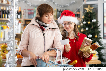Family of mother and daughter with cart shopping at supermarket, looking for something and reviewing and checking list of products to buy. Christmas shopping Family of mother and daughter with cart shopping at supermarket, looking for something and reviewing and checking list of products to buy. Christmas shopping 121139055