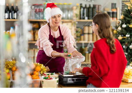 Female employee sells sweets to teen girl, puts candies in bag, puts them on scale and weighs sweets Female employee sells sweets to teen girl, puts candies in bag, puts them on scale and weighs sweets 121139134