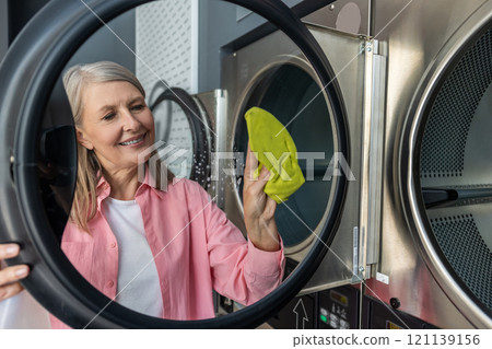 Mature caucasian woman cleaning the washing machine and looking involved 121139156