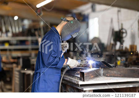 Male welder standing with a welding semi-automatic machine and a safety helmet in metal machining workshop Male welder standing with a welding semi-automatic machine and a safety helmet in metal machining workshop 121139187
