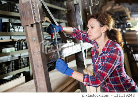 Female employee of workshop stands next to iron rails of workpieces, measures length Female employee of workshop stands next to iron rails of workpieces, measures length 121139248
