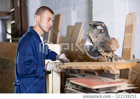 Working at sawmill - man saws wooden board using circular saw Working at sawmill - man saws wooden board using circular saw 121139251