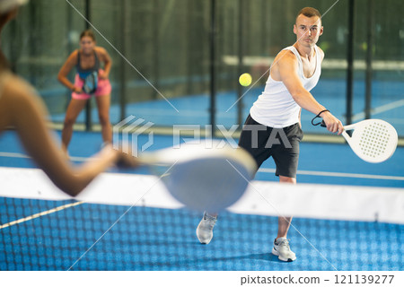 Girl paired with a man plays padel on an indoor tennis court Girl paired with a man plays padel on an indoor tennis court 121139277