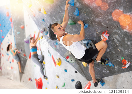 Young man and two women engaged in rock-climbing in indoor hangar 121139314