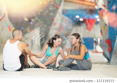 Three climbing friends sit on the floor and discuss options for climbing climbing wall. Share their impressions 121139315