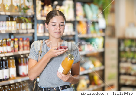 Female shopper scanning QR code on juice bottle in store 121139489