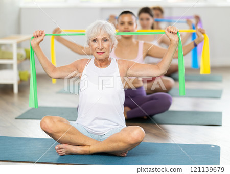 Senior lady performing exercises with resistance band in pilates class 121139679