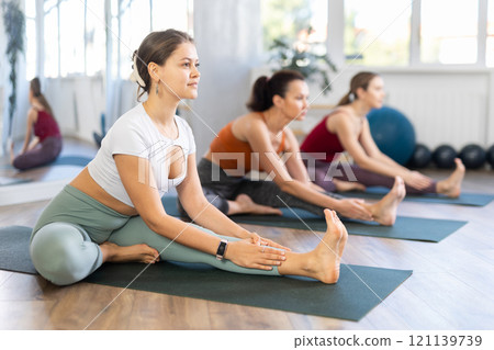 Girl teacher conducts lesson, training for girls in yoga studio and performs Janu Shirshasana. Girl teacher conducts lesson, training for girls in yoga studio and performs Janu Shirshasana. 121139739