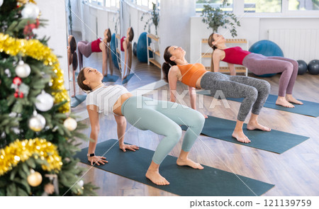 Young woman teacher perform inverted plank with girls in yoga studio in New Year Eve Young woman teacher perform inverted plank with girls in yoga studio in New Year Eve 121139759
