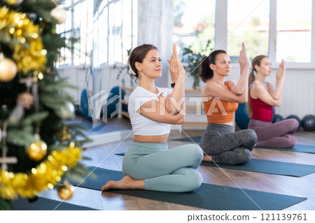 Girl teacher conduct yoga lesson for girls and performs cow head pose in New Year atmosphere 121139761