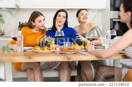 Girlfriends drinking wine and having conversation over dinner at house party 121139819