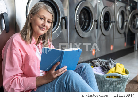 Caucasian mature woman waiting in the laundry and reading something in her diary Caucasian mature woman waiting in the laundry and reading something in her diary 121139914