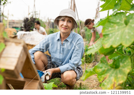 Mature woman sitting at garden bed Mature woman sitting at garden bed 121139951