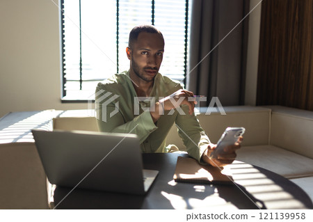 Confident man using laptop and mobile phone while working in office 121139958