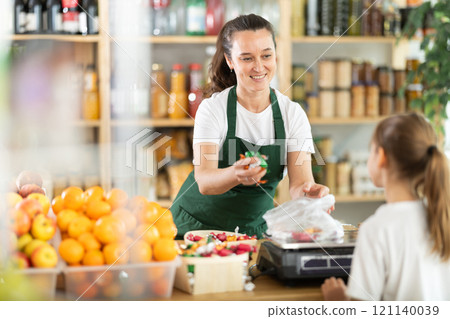 Woman sells sweets to girl, puts candies in bag, puts them on scale and weighs sweets 121140039