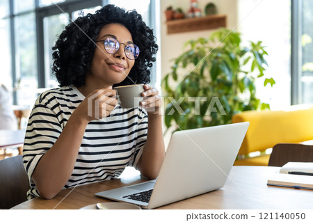 Business woman in striped blouse working on laptop and having coffee Business woman in striped blouse working on laptop and having coffee 121140050