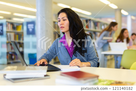 Asian woman student studies in the library on a laptop 121140182
