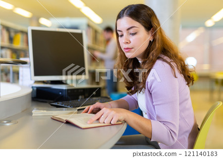 Portrait of woman with laptop and book in public library closeup 121140183