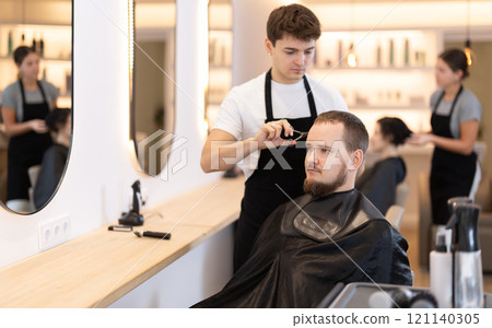 Young guy hairdresser giving haircut to young man 121140305