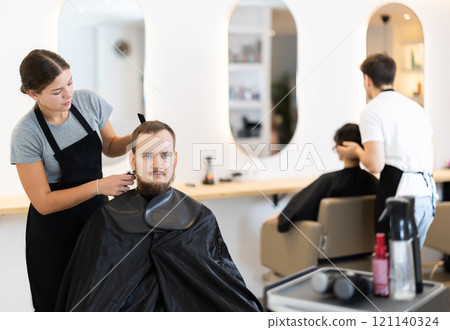 Young female hairdresser giving haircut to young man 121140324