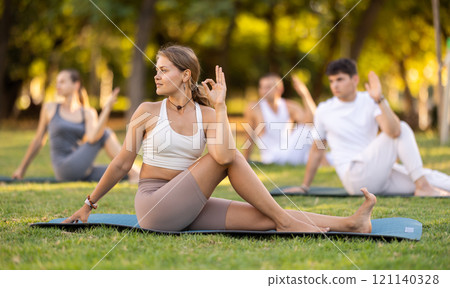 Girl performing twisting asana Matsyendrasana on green meadow 121140328