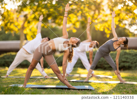 Girl leading outdoor group yoga class in summer park 121140338