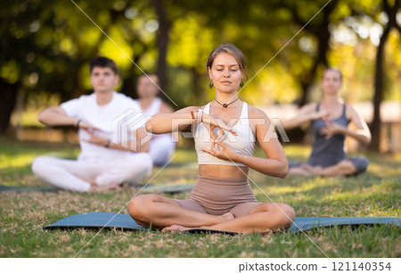 Girl meditating in lotus position during group yoga in park 121140354