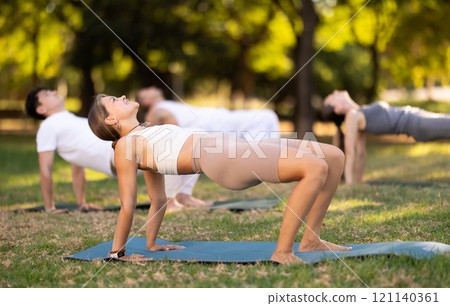 Girl performing Reverse Tabletop Pose during group yoga session in park Girl performing Reverse Tabletop Pose during group yoga session in park 121140361