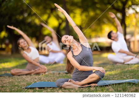 Woman stretching in lotus position during group yoga in park Woman stretching in lotus position during group yoga in park 121140362