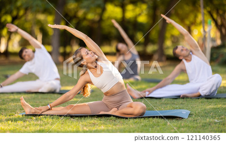 Yoga lesson visitors with coach perform Parivritta Janu Shirshasana in park 121140365
