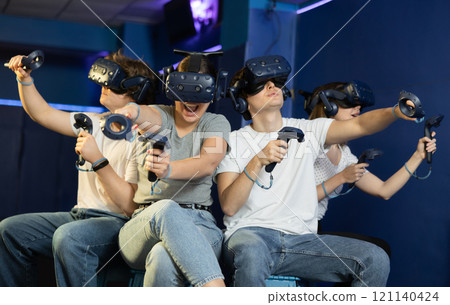 Emotional young girls and guys in VR headsets immersed in game Emotional young girls and guys in VR headsets immersed in game 121140424