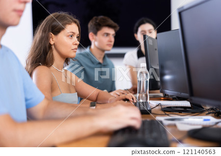 Girl student of computer courses looks at monitor screen, types on keyboard and does work 121140563