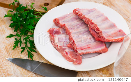 Raw meaty pork ribs slabs on plate with fresh greens Raw meaty pork ribs slabs on plate with fresh greens 121140647