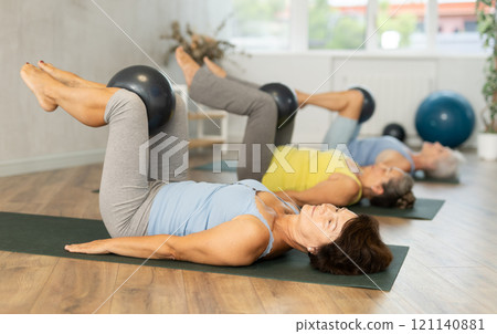 Elderly women perform softball exercises lying on floor, workout for beautiful figure, toned body 121140881