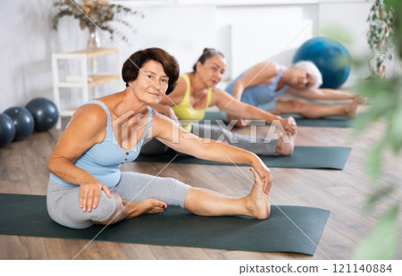 Group of elderly woman doing yoga on mat in studio Group of elderly woman doing yoga on mat in studio 121140884