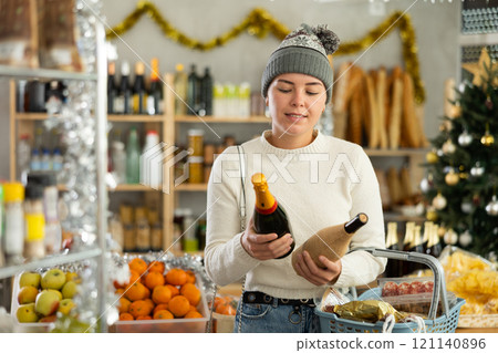 Female shopper chooses between wine and champagne while shopping at supermarket 121140896