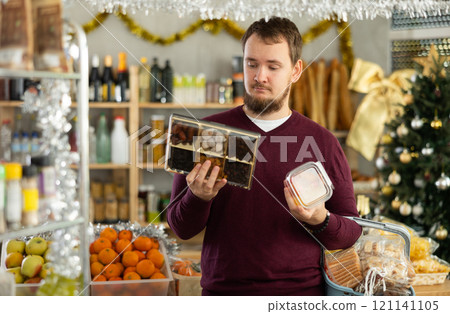 Young bearded man choosing sweets and dried fruits in Christmas decorated store Young bearded man choosing sweets and dried fruits in Christmas decorated store 121141105