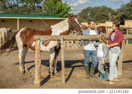 Father, mother and son riding horse together at small horse farm 121141292