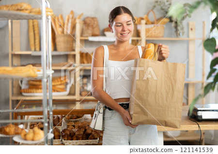 Positive young girl holding baguettes in paper bag in bakery 121141539