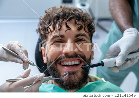 Man patient during visit to the clinic for routine cavity checkup sitting in treatment chair Man patient during visit to the clinic for routine cavity checkup sitting in treatment chair 121141549