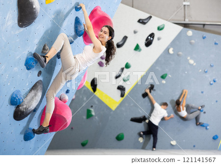 Motivated young girl climbing without ropes and harnesses on artificial bouldering wall in fitness center Motivated young girl climbing without ropes and harnesses on artificial bouldering wall in fitness center 121141567