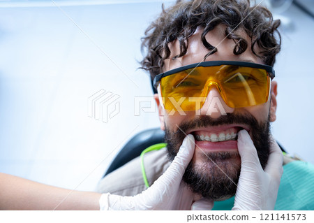 Man patient during whitening teeth procedures in modern dental clinic Man patient during whitening teeth procedures in modern dental clinic 121141573